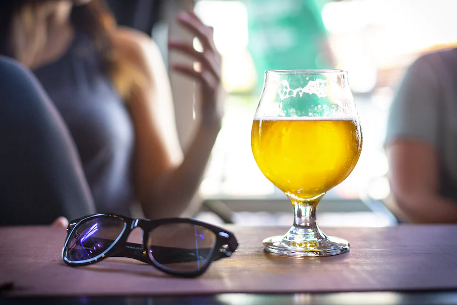 Une bière dans un verre posé sur une table à côté d'une paire de lunettes de soleil